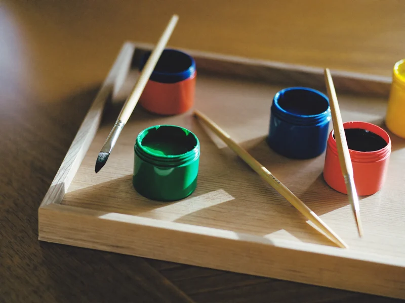 Kleine Modellbaufarben in verschiedenen Tönen mit feinen Pinseln auf einem Holztablett